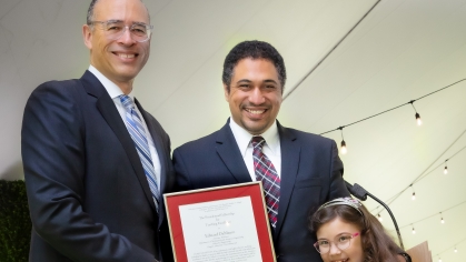 Rutgers University President, Jonathan Holloway on left presenting an award to a male faculty member alongside his young daughter.