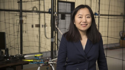 Asian female with long black hair wearing a dark suit standing in a drone lab.