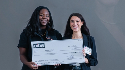 Two women both dressed in black clothing pose holding an oversized check.