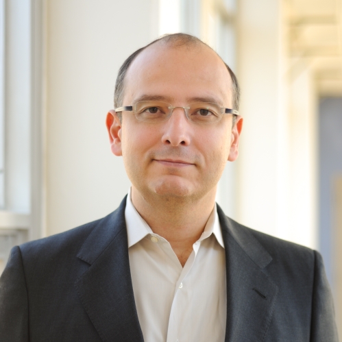 Head shot of balding male with eyeglasses, wearing a black suit jacket and a white button down shirt.