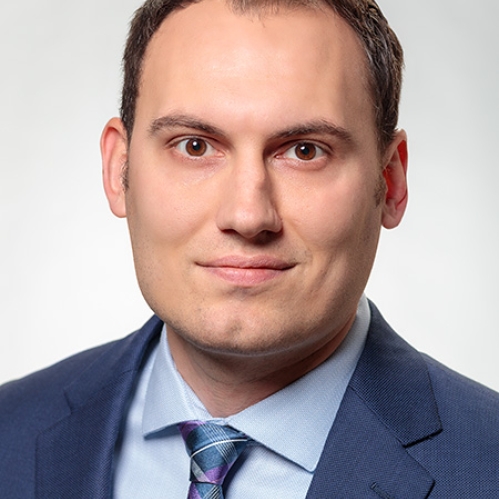 Head shot of male with short hair, wearing a blue suit, blue shirt, and blue tie.