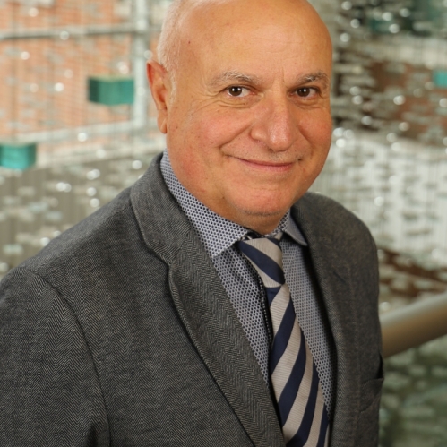 Headshot of bald male wearing a dark grey suit with a grey shirt and striped tie.