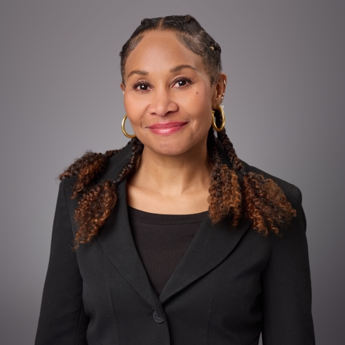 Headshot of Black woman with long dark brown hair wearing gold hoop earrings, a black shirt with a black suit jacket.