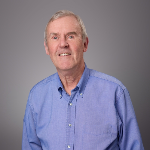 Headshot of male with short white hair wearing a blue button down shirt.