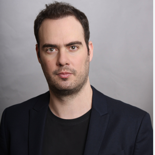 headshot of man with black shirt and jacket on a grey background
