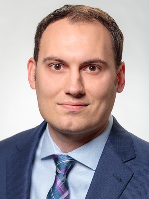 Head shot of male with short hair, wearing a blue suit, blue shirt, and blue tie.
