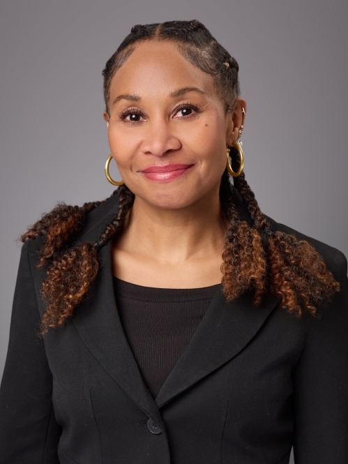 Headshot of Black woman with long dark brown hair wearing gold hoop earrings, a black shirt with a black suit jacket.