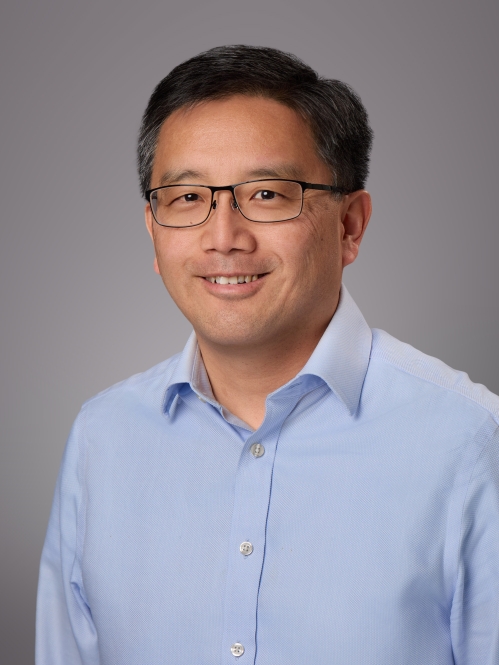 Headshot of male with short black hair and eyeglasses wearing a blue button down dress shirt.