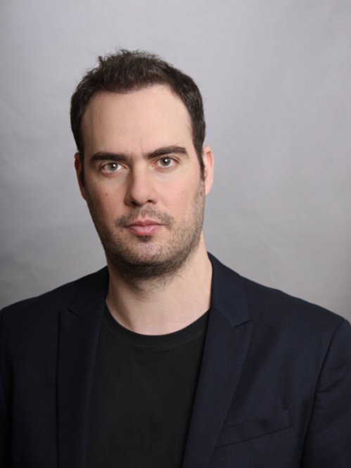 headshot of man with black shirt and jacket on a grey background