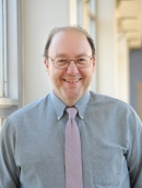 Head shot of balding male with eyeglasses, wearing a pale blue button down shirt and a pink tie.