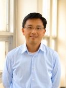 Head shot of Asian male with eyeglasses, wearing a ligh blue button down shirt.