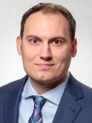 Head shot of male with short hair, wearing a blue suit, blue shirt, and blue tie.