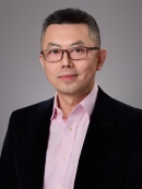 Headshot of male with short black hair and eyeglasses wearing a pink button down shirt and a black suit jacket.