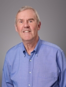 Headshot of male with short white hair wearing a blue button down shirt.