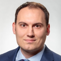 Head shot of male with short hair wearing a blue suit, blue shirt, and blue tie.