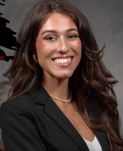Headshot of woman with long brown hair, smiling. She is wearing a black blazer.