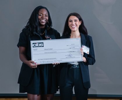 Two women both dressed in black clothing pose holding an oversized check.