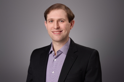 Headshot of male with short hair wearing a black suit jacket and a purple stripped button down shirt.