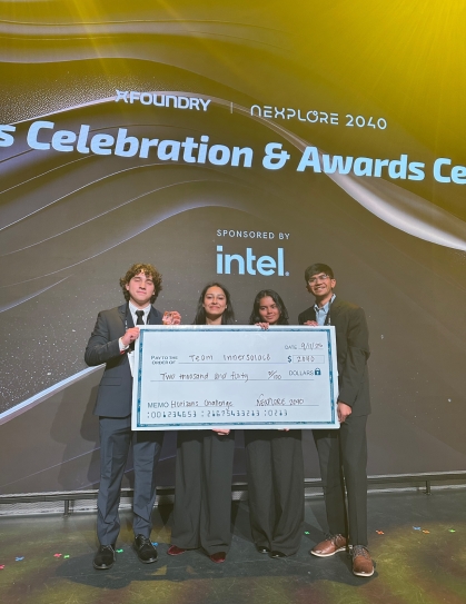 four students holding large blue check in front of black space background