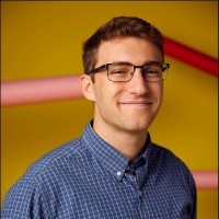 Head shot of male college student with eyeglasses wearing a blue checkered button down shirt.