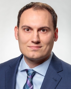 Head shot of male with short hair, wearing a blue suit, blue shirt, and blue tie.